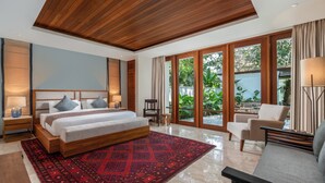 Ein modernes Schlafzimmer mit einem großen Bett, einem Teppich mit rotem Muster und Blick auf einen Garten durch große Fenster.