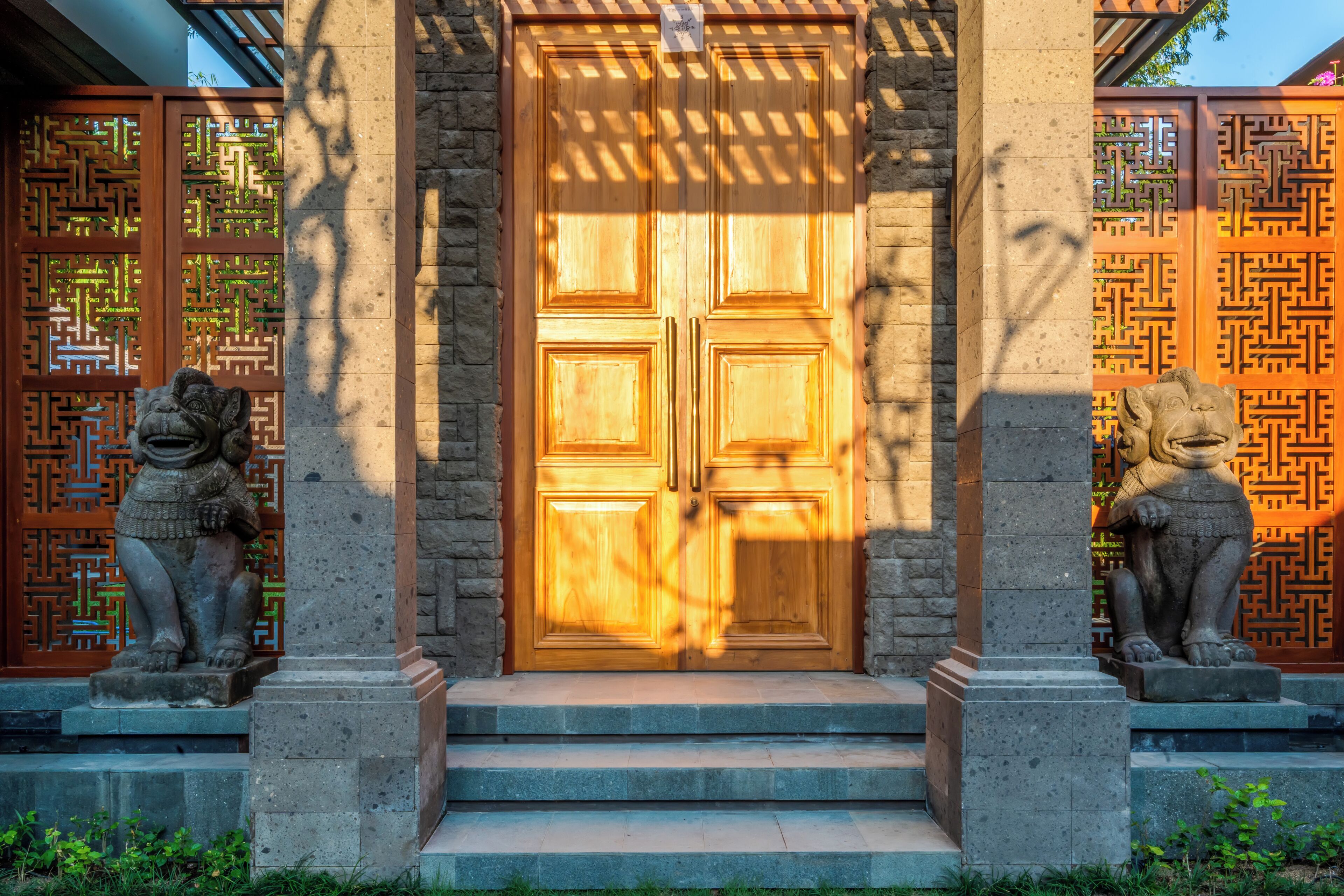 A traditional wooden door with a geometric pattern on the surrounding wall, flanked by stone lion statues.