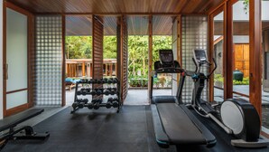 Ein Fitnessraum mit Trainingsgeräten, darunter Laufbänder und Kurzhanteln, und großen Schiebetüren zu einem Außenbereich.