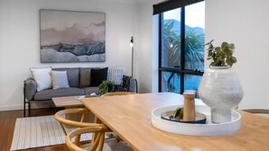 Un salon moderne avec une table à manger en bois, un canapé gris et une grande fenêtre donnant sur des palmiers.