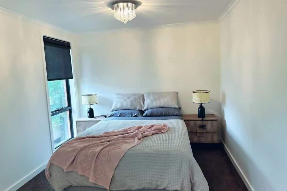 Een slaapkamer met een bed, twee nachtkastjes, een raam en een kroonluchter.