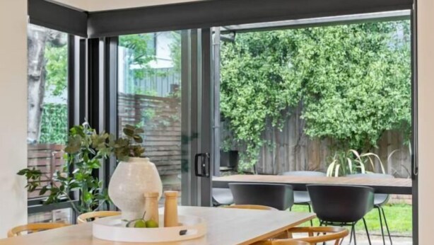 Un espace de repas moderne avec une table et des chaises en bois, un vase avec des plantes et une vue sur un jardin avec des arbres.