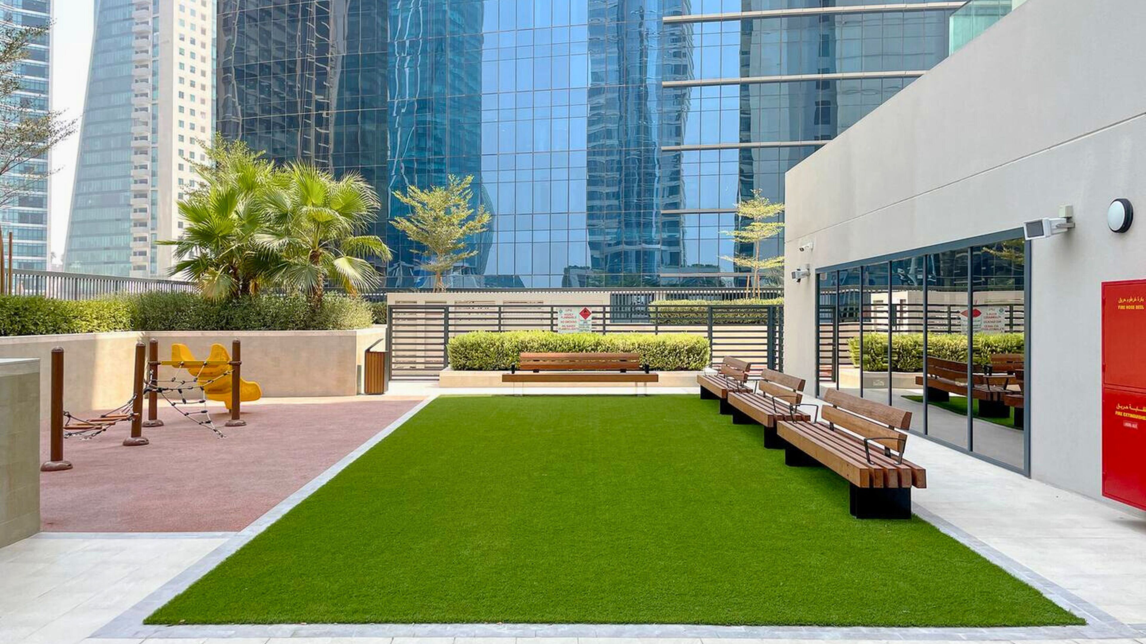 An outdoor area with artificial grass, benches, and a playground with a climbing structure.