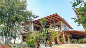 A two-story house with a balcony, surrounded by potted plants and trees. - Keith Ratchaburi (Ban Pong)