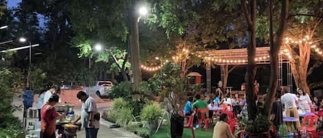 Un espacio al aire libre para comer con mesas y sillas, rodeado de árboles y luces colgantes.