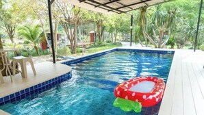A swimming pool with a red mushroom float, surrounded by a covered deck and lush greenery. - Keith Ratchaburi (Ban Pong)