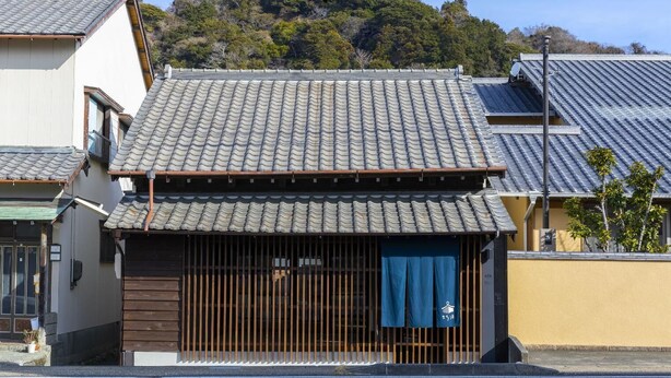 A traditional Japanese building with a tiled roof, wooden slats, and a blue curtain.