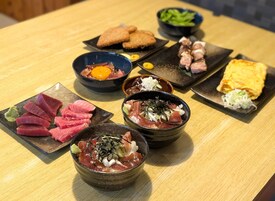 Variedad de platos sobre una mesa de madera, incluyendo sashimi, un cuenco de huevo y otros alimentos.