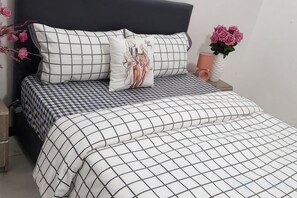 A bed with a checkered bedspread and pillows, a vase with flowers, and a nightstand with a lamp. - Erykah Hotel Mityana Road (Mawokota)