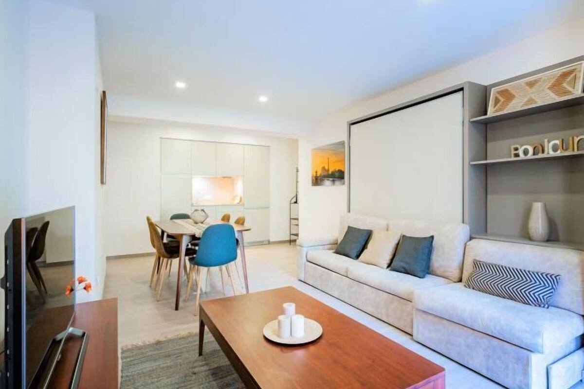 Una sala de estar moderna con un sofá, una mesa de centro, un televisor y un comedor con sillas y una mesa.