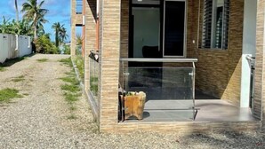 Un edificio moderno con puerta de entrada de vidrio, un pequeño espacio de asientos al aire libre y vistas a palmeras.