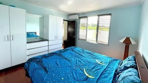 Un dormitorio con cama, armario, ventana con persianas y aire acondicionado.