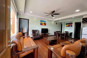 A spacious living area with leather sofas, a dining table, and a ceiling fan. - Affordable Apartment 3 Bedrooms (Suva)