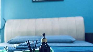 Una cama con una manta azul, un almohadón blanco y un frasco negro con dispensador.