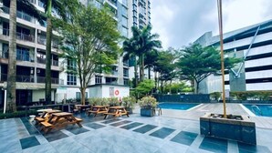 A courtyard with outdoor seating, a pool, and modern buildings in the background. - Johor Cozy Home 2 Rooms & Easy Parking Fast WiFi ! (Plentong)
