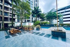 A courtyard with outdoor seating, a pool, and modern buildings in the background. - Johor Cozy Home 2 Rooms & Easy Parking Fast WiFi ! (Plentong)