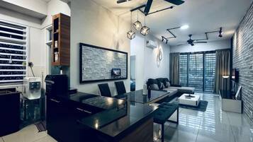 A modern kitchen with a central island, a dining area with a glass table, and a living space with a sofa and a TV.