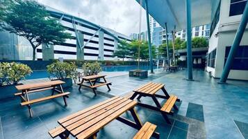 Een terras buiten met houten picknicktafels en banken, omringd door gebouwen en begroeiing.