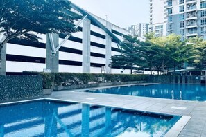 A swimming pool with a tiled deck, surrounded by greenery and modern buildings. - Johor Cozy Home 2 Rooms & Easy Parking Fast WiFi ! (Plentong)