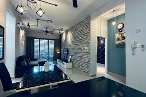 A modern living room with a black marble dining table, a sofa, a TV, and a stone wall. - Johor Cozy Home 2 Rooms & Easy Parking Fast WiFi ! (Plentong)