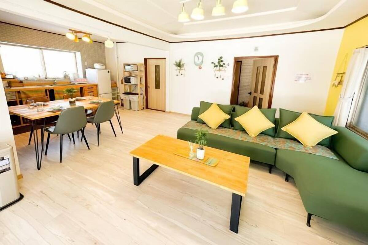 A modern living room with a green sofa, a wooden coffee table, and a dining area with chairs and a table.