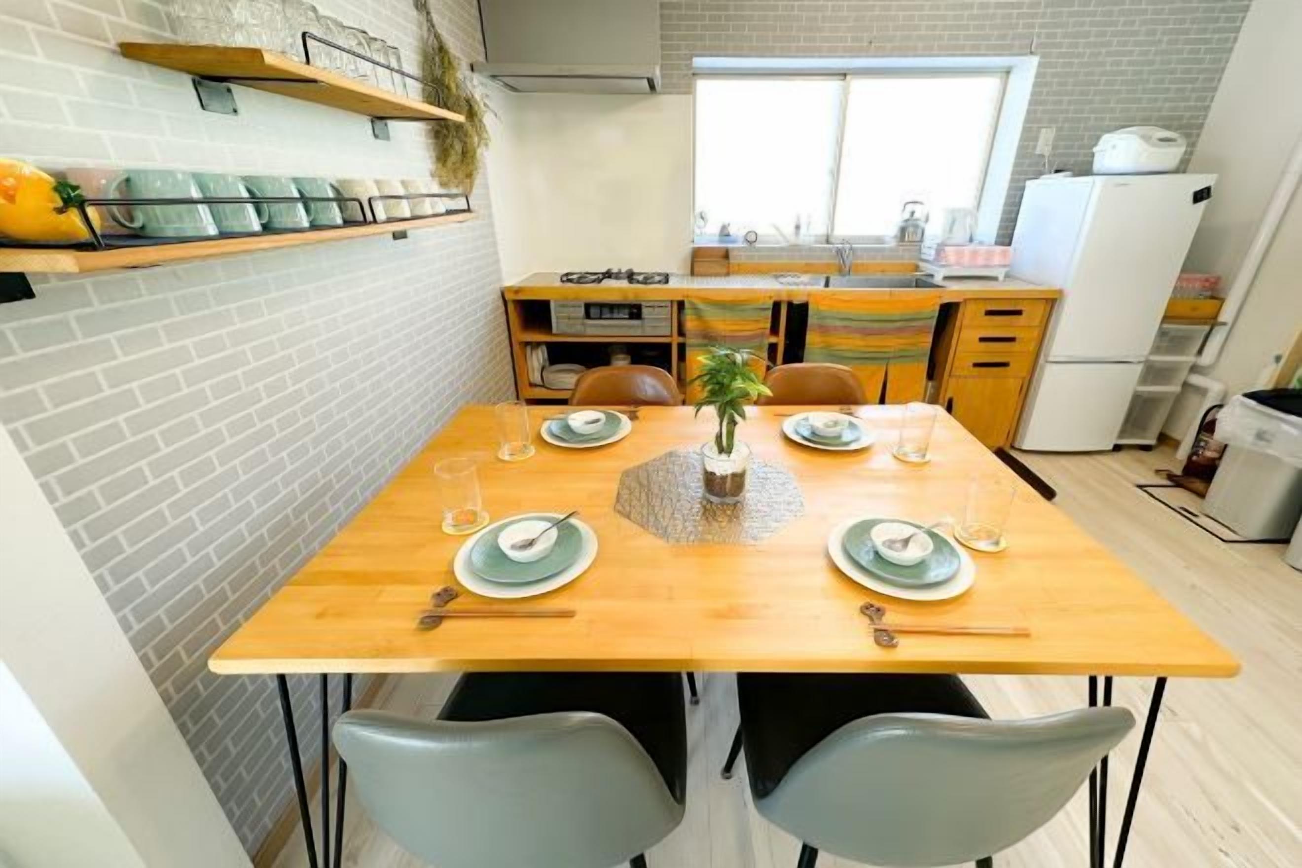 A dining area with a wooden table set for four, surrounded by grey chairs. A small plant is placed in the center of the table.