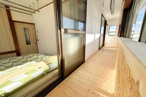 A narrow corridor with a bed on the left, a sliding door, and a wooden floor. - Mintmint (Noboribetsu)