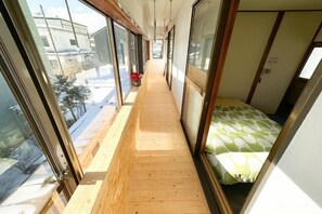 A narrow corridor with a wooden floor, large windows, and a bed with a green and white patterned bedspread. - Mintmint (Noboribetsu)
