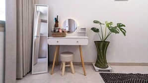 Een kamer met een wit aanrichtmeubel, een ronde spiegel, een krukje, een plant in pot en een gestreept vloerkleed.