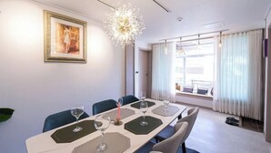 Een moderne hotelkamer met een eethoek, bestaande uit een lange tafel, meerdere stoelen en een groot raam met gordijnen.