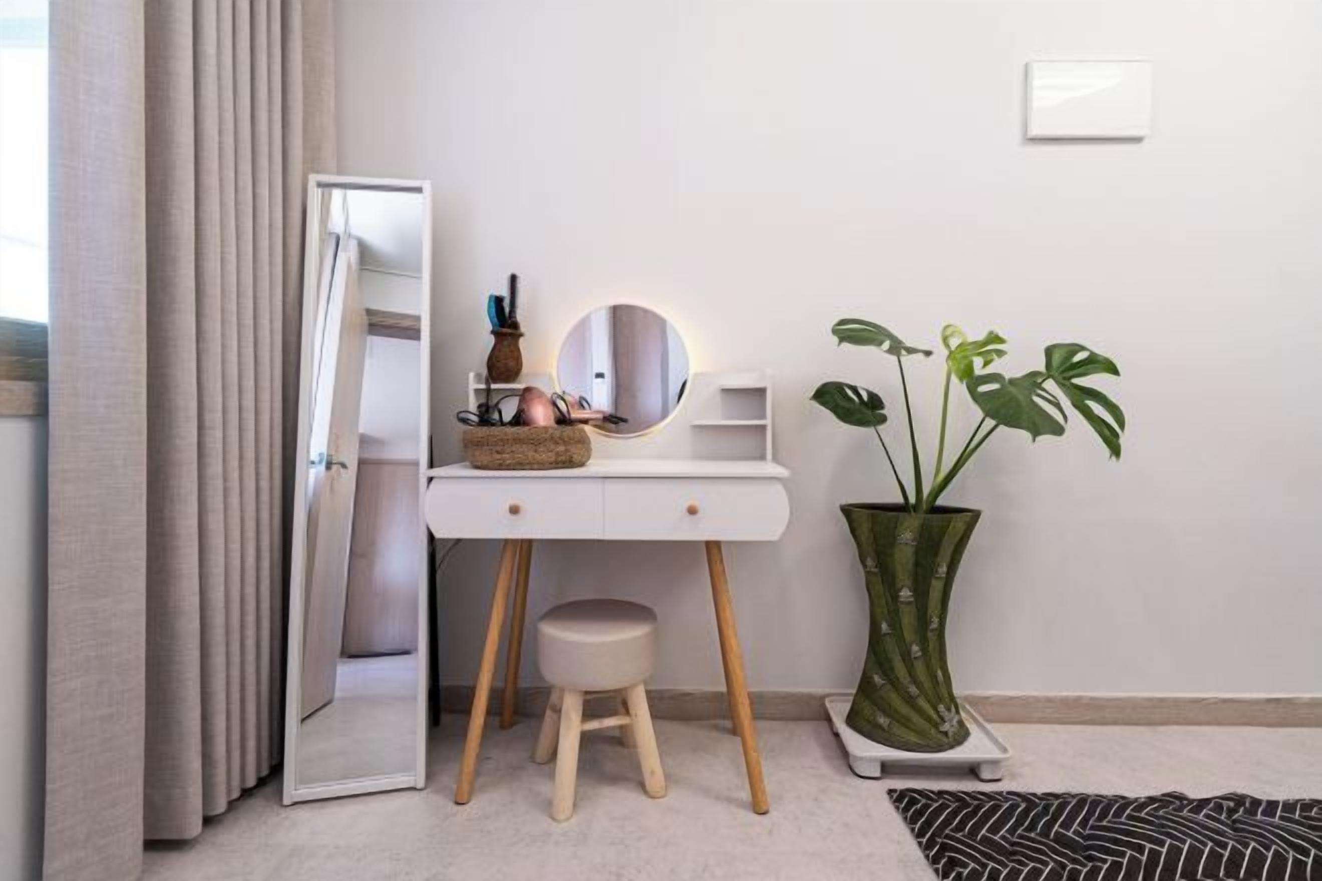 A room with a white desk, a mirror, a small stool, a potted plant, and a door.