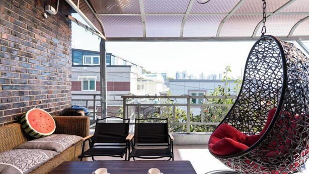 Een balkon met een hangstoel, een tafel met kopjes en een bakstenen muur.