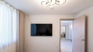 Hotelkamer met een bed, een aan de muur bevestigde televisie, een deur en zicht op een andere kamer.