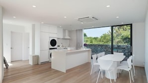 Une cuisine moderne avec des meubles blancs, un îlot central et un coin repas avec des chaises blanches.