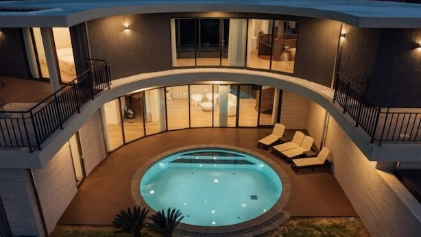 Une maison moderne dotée d’une piscine circulaire, d’un patio couvert avec des sièges et d’un balcon agrémenté d’une balustrade.