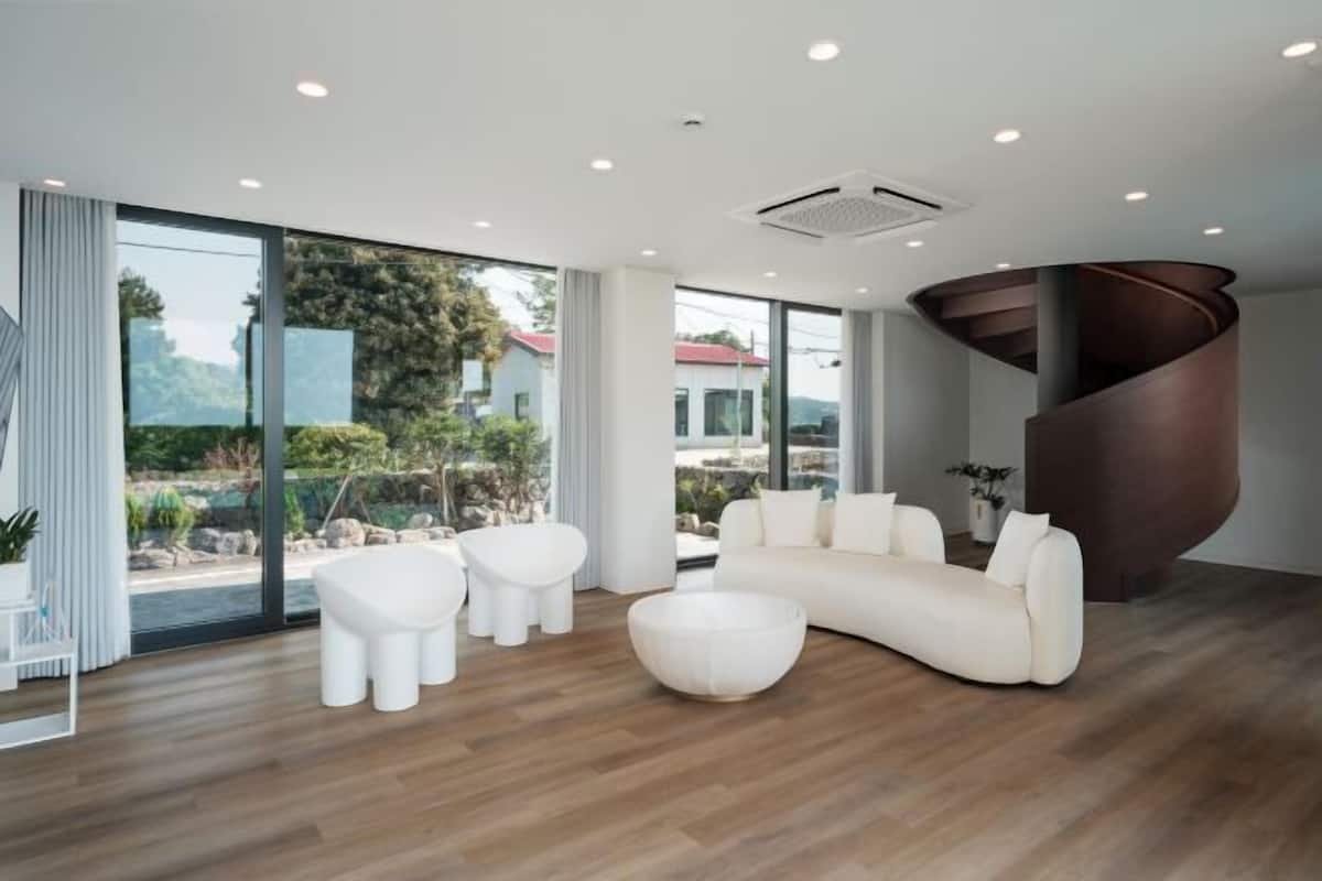 A modern living room with a curved staircase, large windows, and a wooden floor.