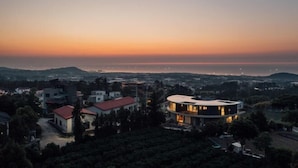 Une maison moderne à l’architecture circulaire originale, entourée d’un paysage verdoyant luxuriant et offrant une vue sur la mer au coucher du soleil.