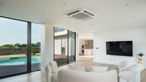 Un salon moderne doté d’un grand téléviseur, de meubles blancs et offrant une vue sur une piscine.