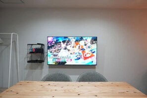 Een vergaderruimte met een groot scherm aan de muur waarop een spel wordt getoond, een houten tafel en twee stoelen.