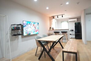 Um espaço de estar moderno com uma mesa de jantar, cadeiras, TV e cozinha.