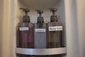 Drie flessen shampoo, conditioner en douchegel in een badkamerkast.