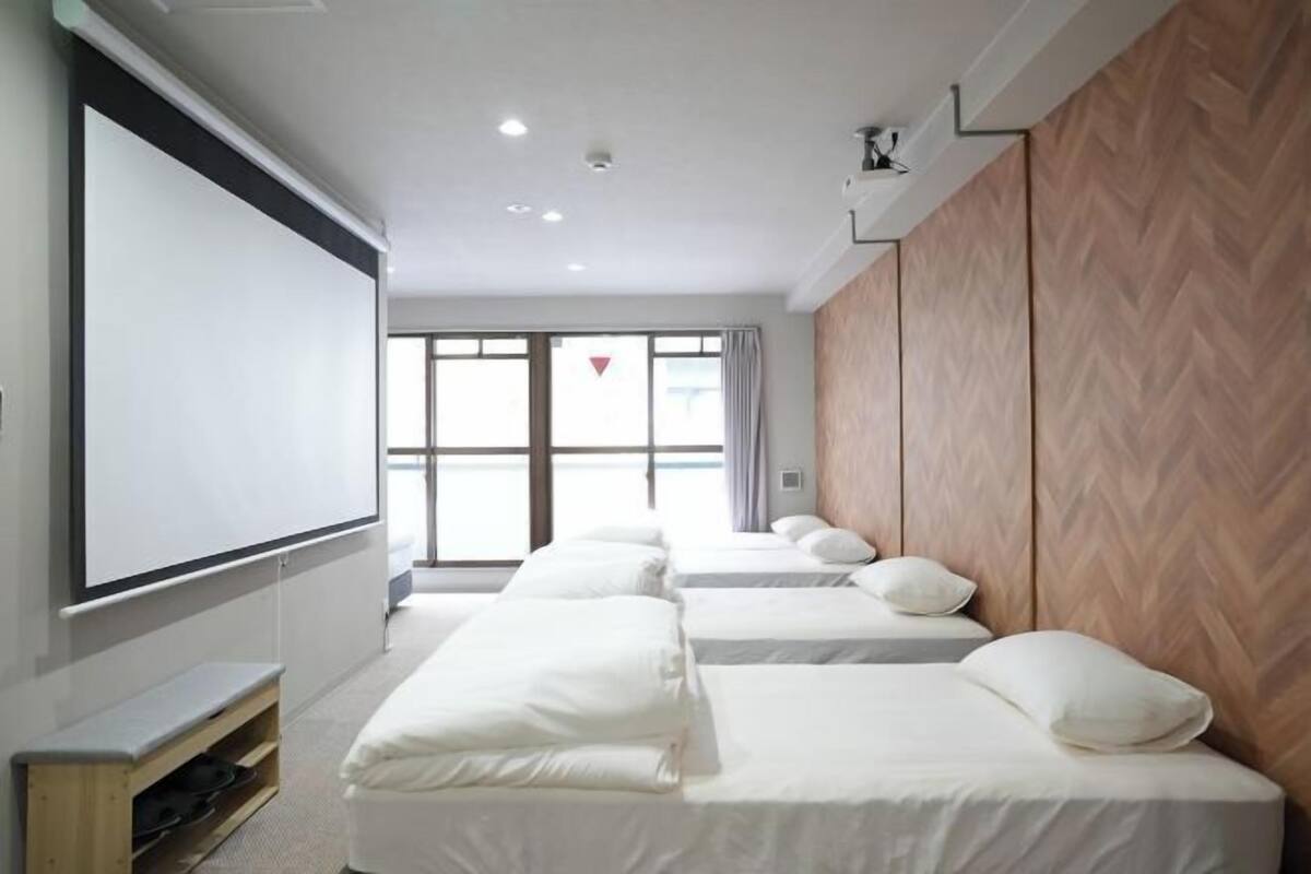 A hotel room with a large bed, a smaller bed, a TV screen, and a wooden wall.