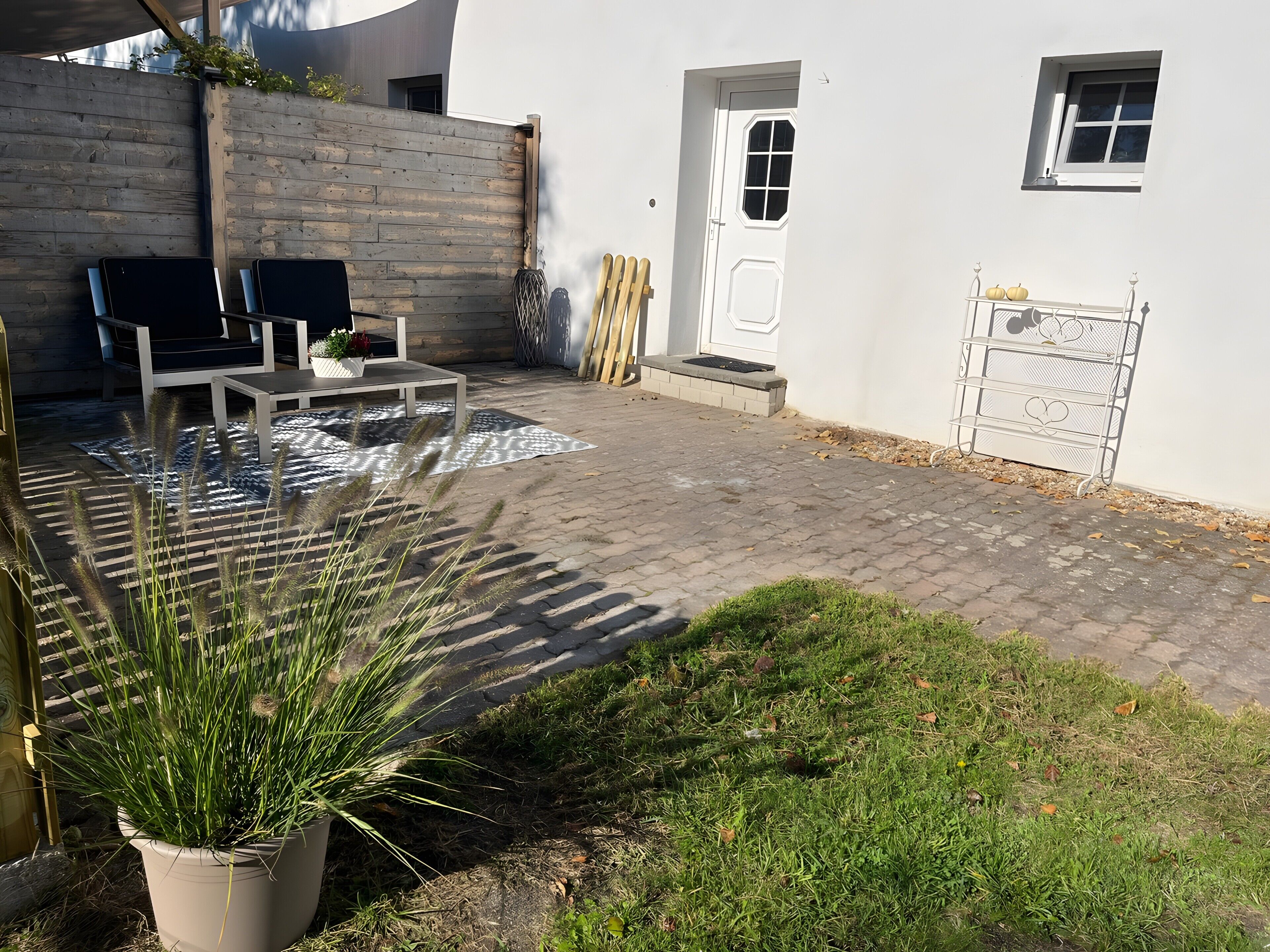 Eine Terrasse mit Gartenmöbeln, einem Blumentopf und einer weißen Wand mit Tür und Fenster.