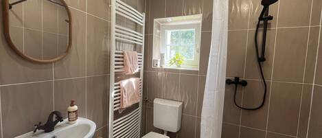 Baño con lavamanos, inodoro, toallero, ducha y ventana con planta.