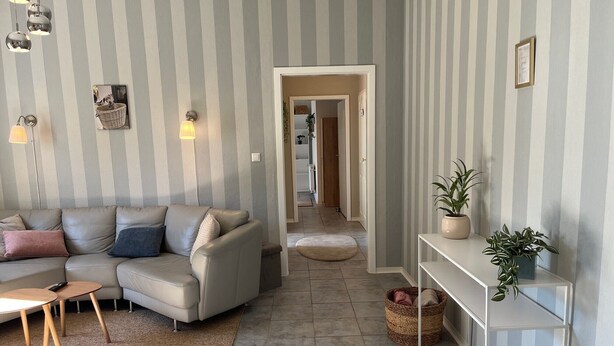 A living room with a sofa, a small table, a rug, a potted plant, and a hallway leading to another room. - Holiday Apartment at Conradhof 2 with Garden and Nature Views (Goch)