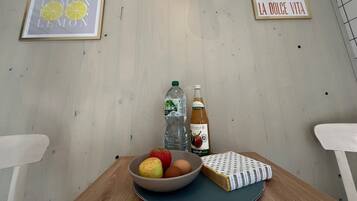 A room with a wooden table, a bowl of fruit, a bottle of water, a bottle of wine, and two framed pictures on the wall.
