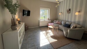 A living room with a sofa, a TV, a potted plant, and a window. - Holiday Apartment at Conradhof 2 with Garden and Nature Views (Goch)