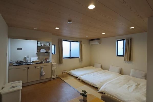 A hotel room with a kitchenette, two beds, a small table, and a window.