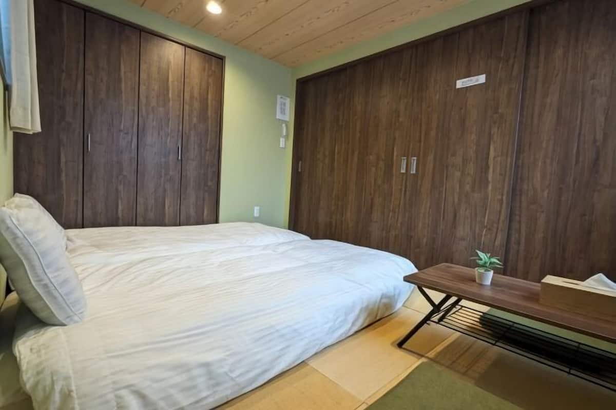 Een slaapkamer met een bed, een houten garderobe en een klein tafeltje met een plant.