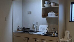A kitchen with a sink, stove, and various utensils. There are cabinets below the counter and a shelf above it with dishes and a basket. - Private Villa Tofukuji (Kyoto)